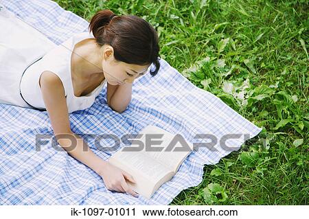 Stock Image - Young Woman Laying Down Reading a Book. Fotosearch