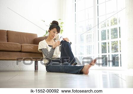 Stock Image - Young woman leaning by sofa and listening music. Fotosearch
