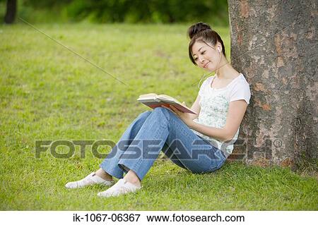 Young woman listening music leaning against tree View Large Photo Image Stock Photo - Young woman listening music leaning against tree. Fotosearch