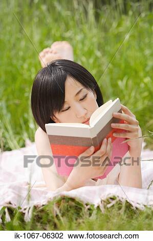 Stock Image - Young woman lying on grass and reading book. Fotosearch