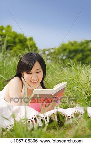 Young woman lying on grass and reading book View Large Photo Image Stock Photograph - Young woman lying on grass and reading book. Fotosearch