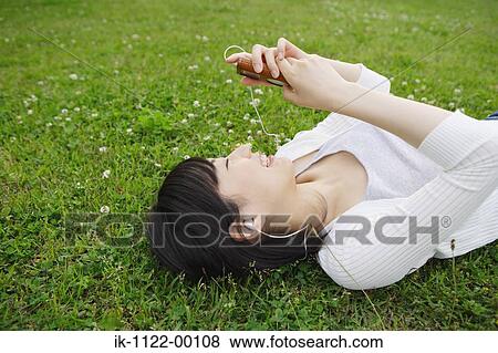 Young woman lying on grass and listening music View Large Photo Image Stock Photo - Young woman lying on grass and listening music. Fotosearch