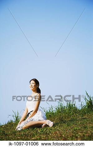 Stock Photograph - Young Woman Sitting Down on Grassy Hill. Fotosearch