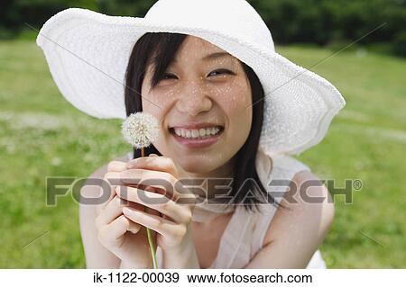 Stock Photo - Young woman smiling and holding dandelion flower. Fotosearch
