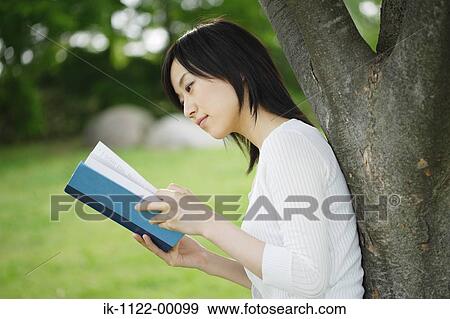 Stock Photo - Young woman studying by tree. Fotosearch