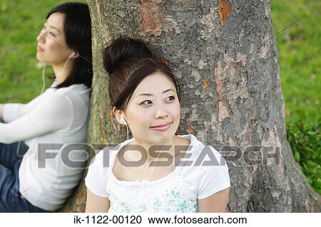Young Women listening music leaning by tree View Large Photo Image Stock Image - Young Women listening music leaning by tree. Fotosearch