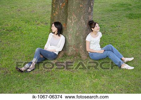 Young women listening music leaning against tree View Large Photo Image Picture - Young women listening music leaning against tree. Fotosearch
