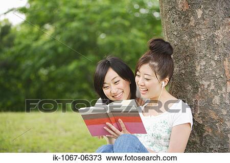 Young women listening music leaning against tree View Large Photo Image Stock Image - Young women listening music leaning against tree. Fotosearch