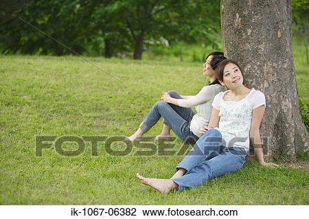 Young women listening music leaning against tree View Large Photo Image Stock Image - Young women listening music leaning against tree. Fotosearch