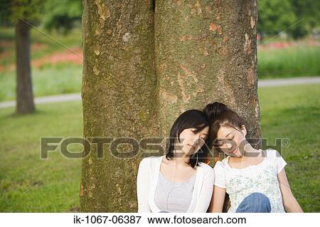 Young women listening music leaning against tree View Large Photo Image Stock Photo - Young women listening music leaning against tree. Fotosearch