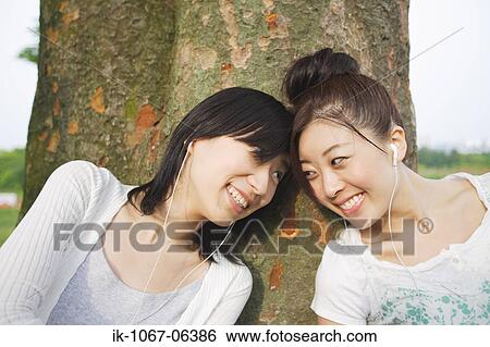 Young women listening music leaning against tree View Large Photo Image Stock Photograph - Young women listening music leaning against tree. Fotosearch