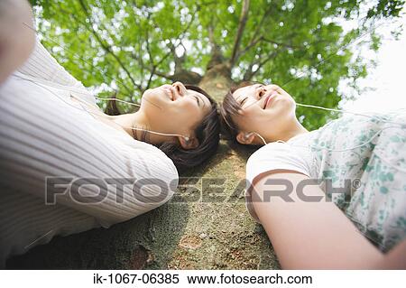 Stock Photography - Young women listening music leaning against tree. Fotosearch