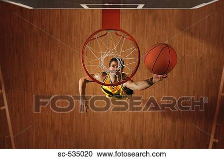 Stock Image - Basketball player slam dunking ball in hoop. Fotosearch