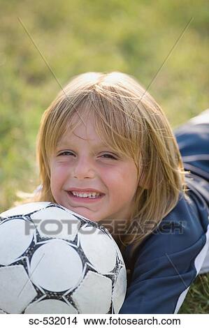 Boy lying on ground with his chin resting on a soccer ball View Large Photo Image Picture - Boy lying on ground with his chin resting on a soccer ball. Fotosearch
