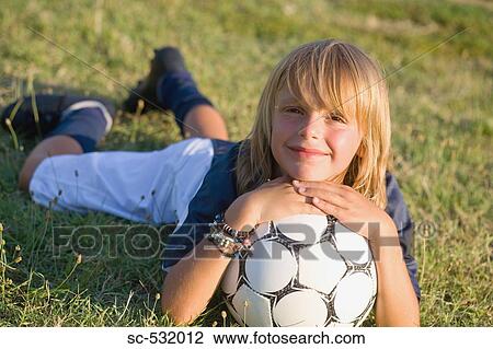 Stock Image - Boy smiling and lying on grass with soccer ball. Fotosearch