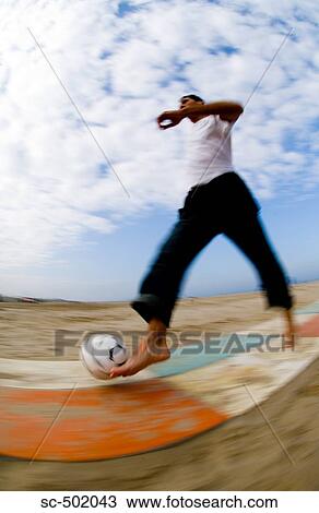 Stock Image - Caucasian male playing with soccer ball on beach. Fotosearch