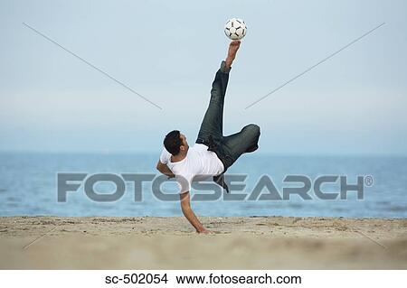 Picture - Caucasian male practicing soccer on beach. Fotosearch