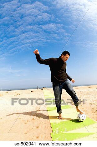 Stock Image - Caucasian male practicing soccer on beach. Fotosearch