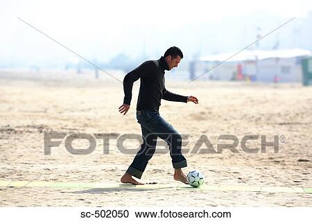 Stock Image - Caucasian male practicing soccer on beach. Fotosearch