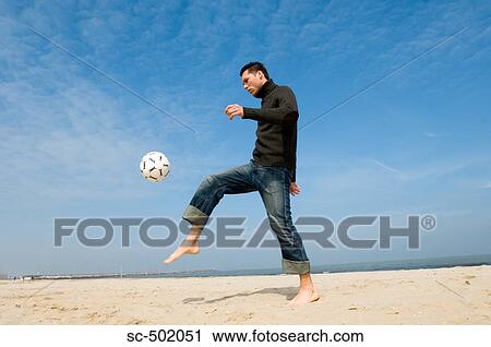 Stock Image - Caucasian male practicing soccer on beach. Fotosearch