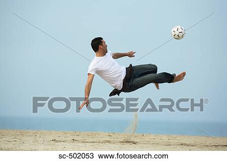 Stock Image - Caucasian male practicing soccer on beach. Fotosearch