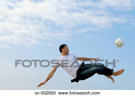 Stock Photography - Caucasian male practicing soccer on beach. Fotosearch