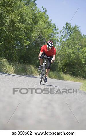 Stock Image - Front view of a man cycling on road. Fotosearch