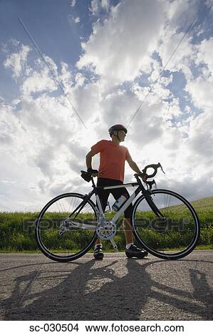 Picture - Front view of a man standing on road with bicycle. Fotosearch