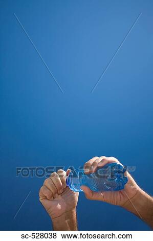 Stock Photo - Hands of a person holding water bottle against blue sky. Fotosearch