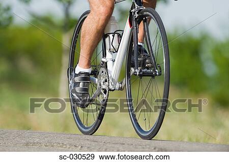 Stock Photo - Low section of a man cycling on road. Fotosearch