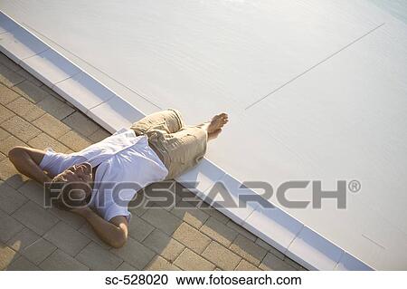 Stock Image - Man relaxing at the edge of pool. Fotosearch