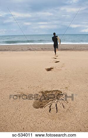 Stock Image - Man running on sand towards sea with leaving his footprints on beach. Fotosearch