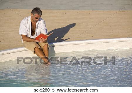 Stock Photography - Man sitting at edge of pool and reading book. Fotosearch