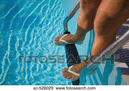 Stock Photo - Man standing on the pool ladder of the swimming pool. Fotosearch