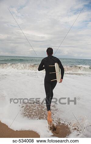 Stock Photo - Man walking into the sea holding his surfboard. Fotosearch