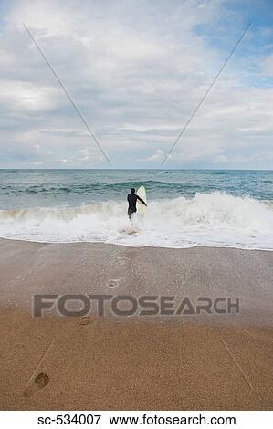 Stock Photo - Man walking into the sea with surfboard. Fotosearch