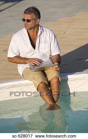 Stock Photo - Man with laptop by swimming pool. Fotosearch