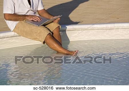 Stock Photograph - Man with laptop by swimming pool. Fotosearch