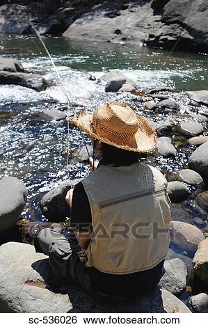 Man with straw hat sitting on stone and fishing View Large Photo Image Stock Photograph - Man with straw hat sitting on stone and fishing. Fotosearch