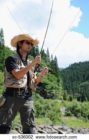 Stock Image - Man with straw hat standing and holding fishing rod. Fotosearch
