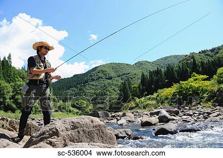 Picture - Man with straw hat standing on stone and holding fishing rod. Fotosearch
