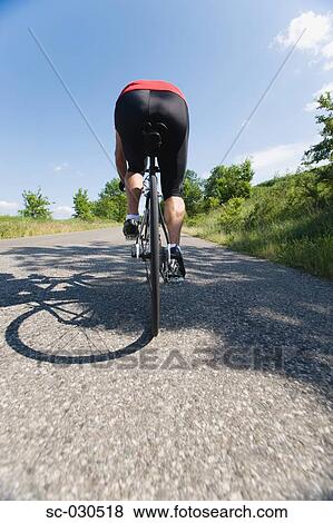 Rear view of a man cycling on road View Large Photo Image Stock Photo - Rear view of a man cycling on road. Fotosearch