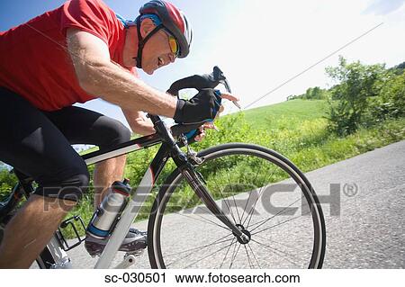Stock Image - Side view of a man cycling on road. Fotosearch