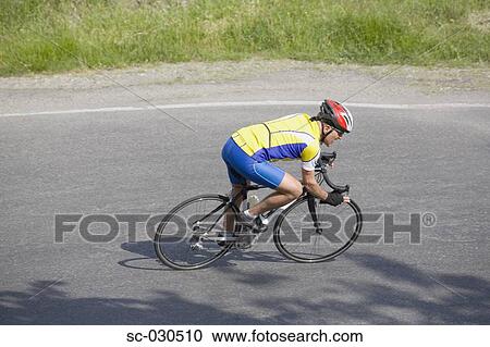 Stock Image - Side view of a man cycling on road. Fotosearch