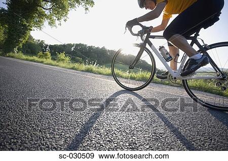Side view of a man cycling on road View Large Photo Image Stock Photo - Side view of a man cycling on road. Fotosearch