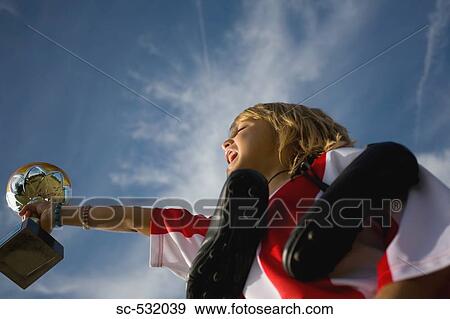 Stock Photo - Soccer player holding shoes, trophy and shouting. Fotosearch