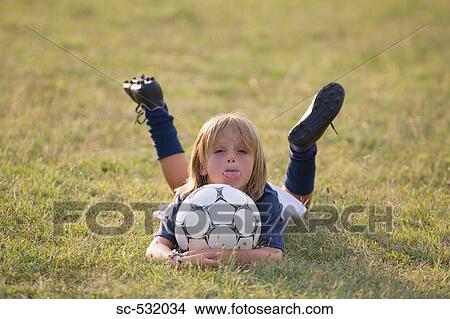 Picture - Soccer player lying on front and holding football. Fotosearch