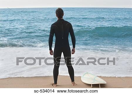 Surfer in wetsuit standing on beach View Large Photo Image Picture - Surfer in wetsuit standing on beach . Fotosearch