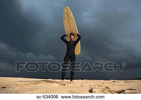 Surfer standing on beach and holding surfboard above his head View Large Photo Image Stock Photograph - Surfer standing on beach and holding surfboard above his head. Fotosearch
