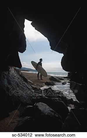 Stock Image - Surfer standing on beach with his surfboard. Fotosearch
